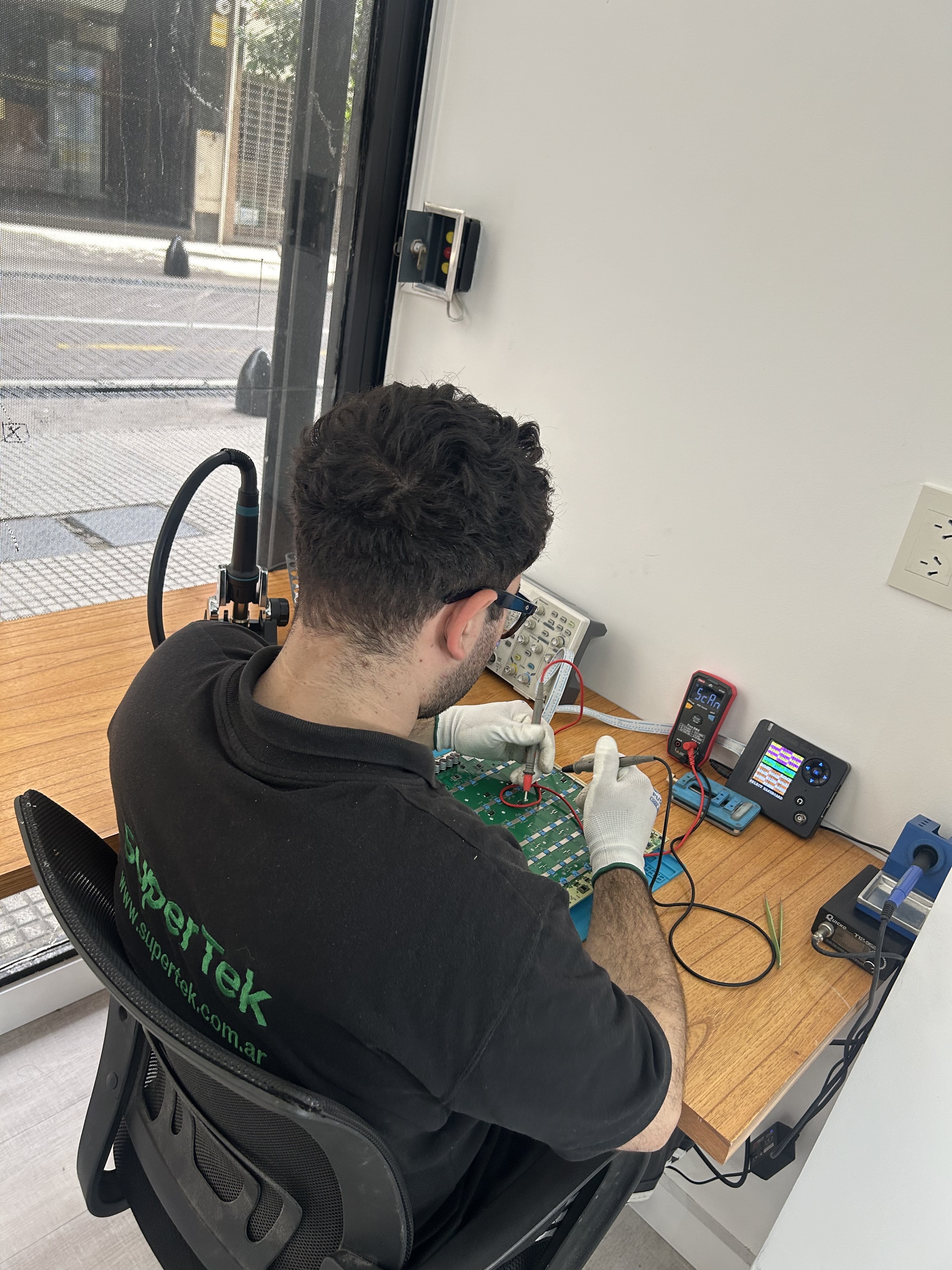 Técnico de Supertek midiendo una hashboard con puntas de multímetro en el banco de trabajo del taller